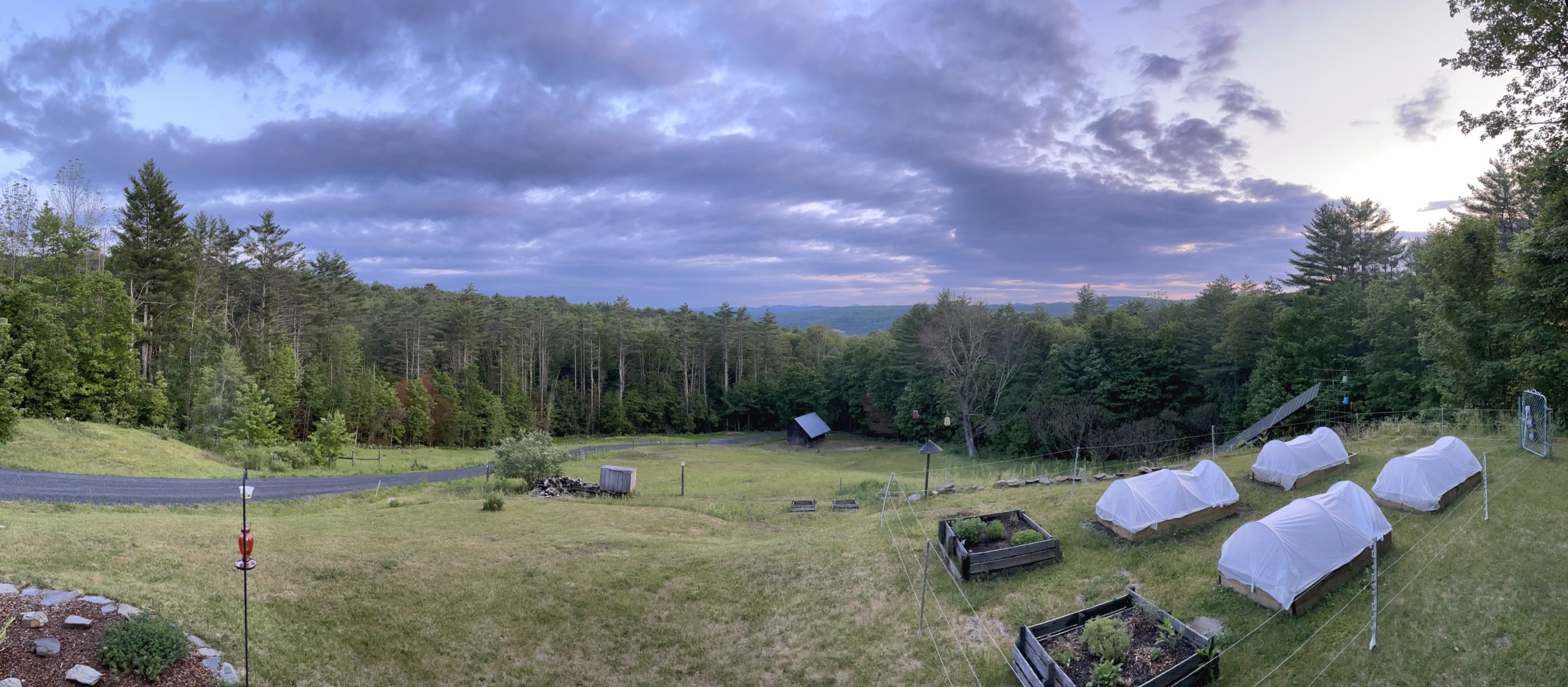 A panoramic photo taken from our front porch with lots of clouds, sky and trees.
